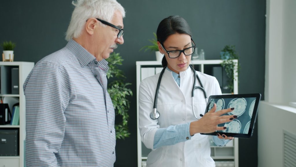 Young woman in uniform is showing patient MRI images on tablet screen talking holding gadget. People, healthcare and modern devices concept.