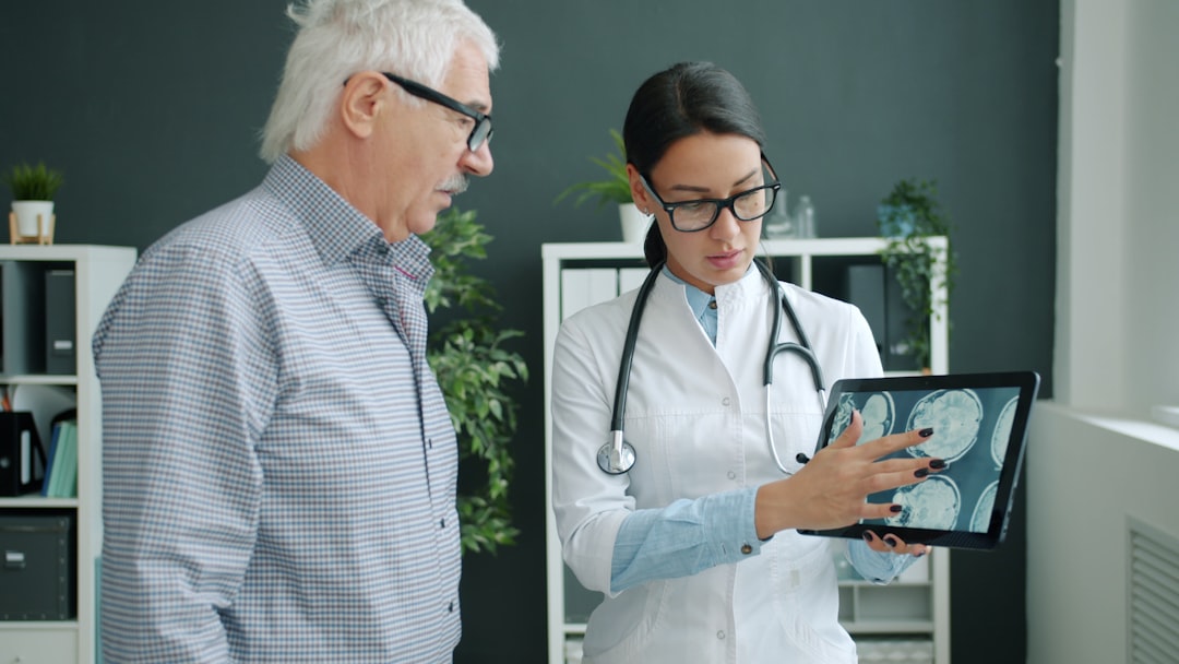 Young woman in uniform is showing patient MRI images on tablet screen talking holding gadget. People, healthcare and modern devices concept.